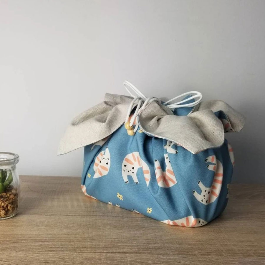 A soft blue bag with a cute design of white cats with orange markings.