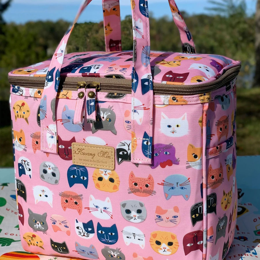 A big pink, rectangular bag with different colorful cat heads.